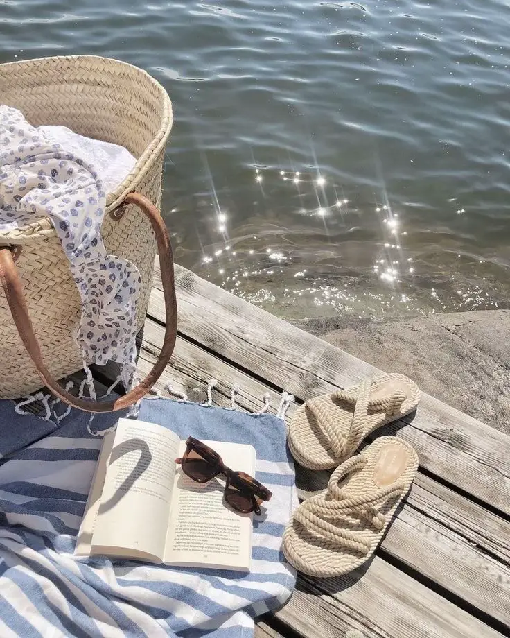  A basket is sitting on a dock with a book and a pair of shoes inside.