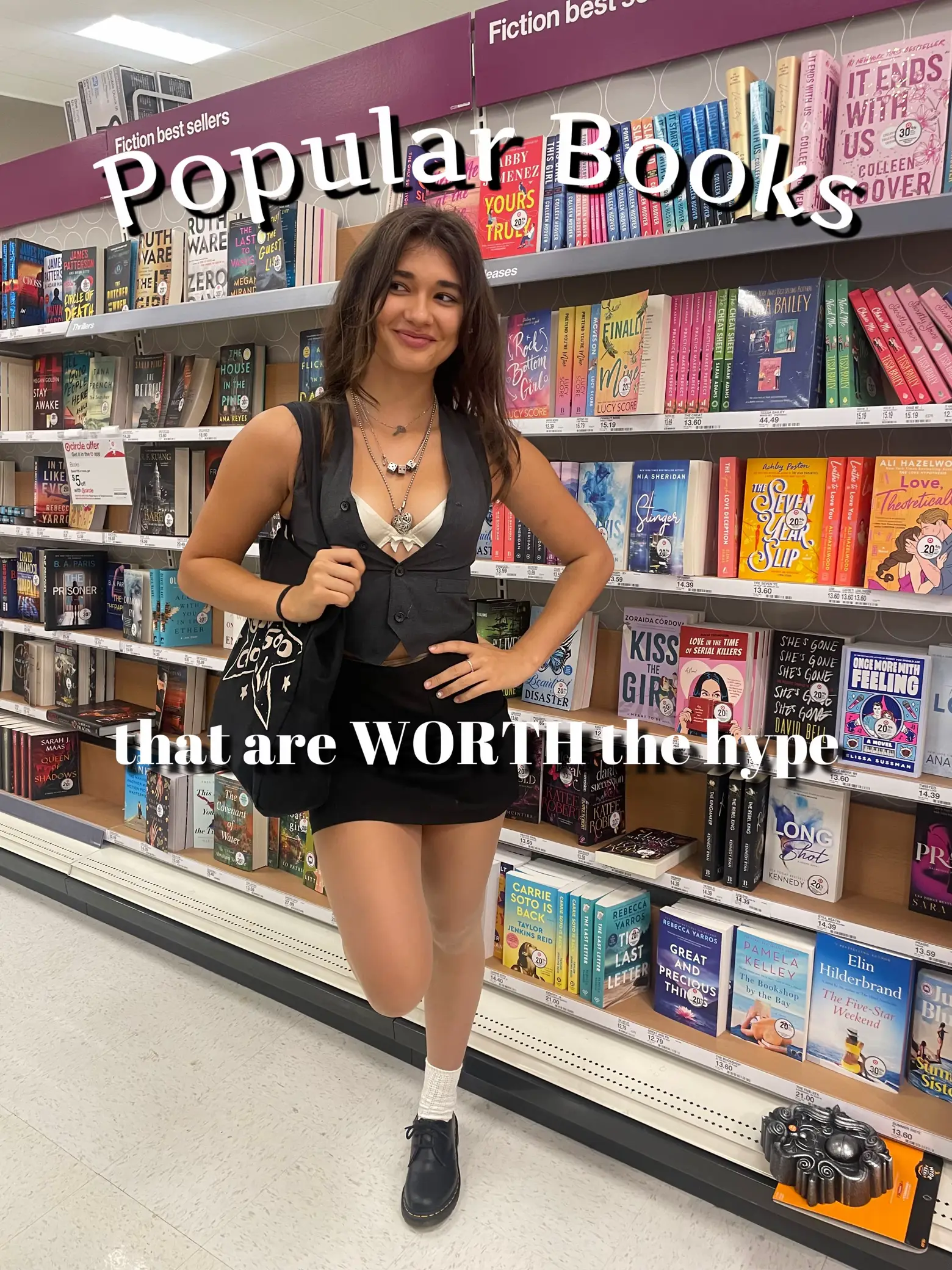  A woman wearing a black dress and a necklace is standing in a bookstore. She is holding a purse and has her hand on her hip. The store has a variety of books on display, with some placed in the foreground and others in the background. The woman appears to be posing for a picture in the store, and the books are arranged in a way that they are easily visible. The woman is smiling and appears to be enjoying her time in the store.