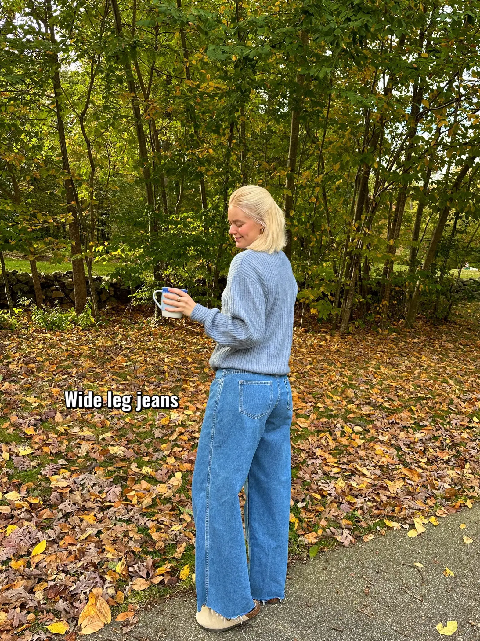  A woman wearing a sweater and jeans is standing in a field.