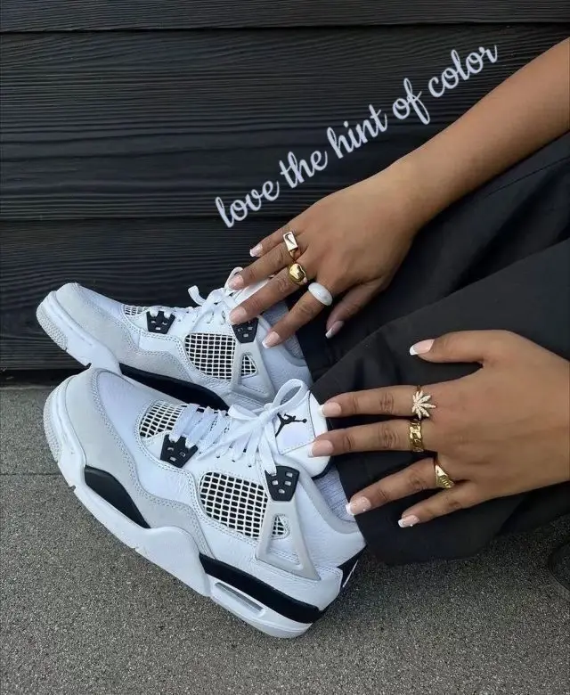  A hand with a ring on the finger is sitting on a pair of grey Nike Air Force One shoes.