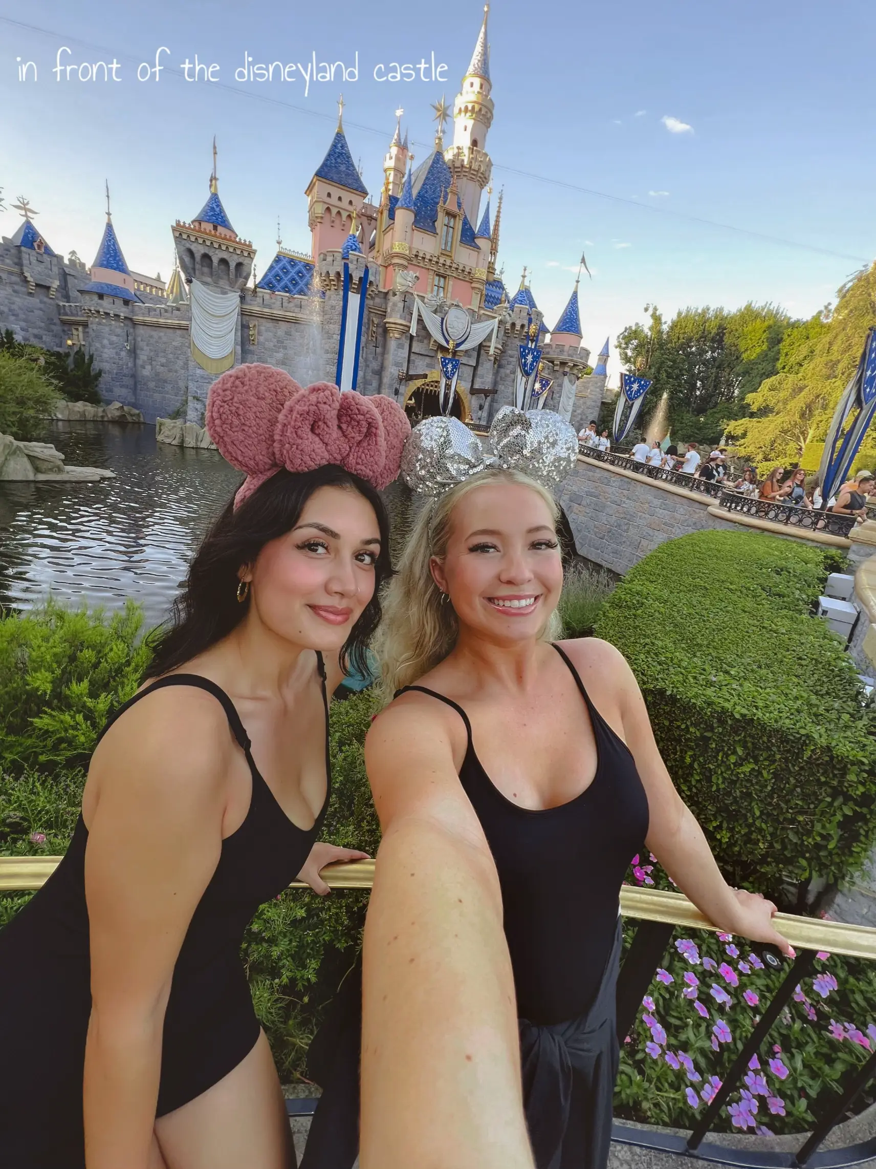  Two women wearing black dresses and pink hats are taking a selfie in front of a castle.