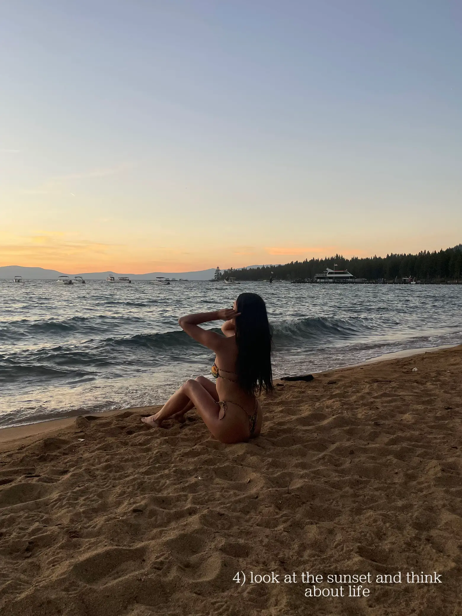  A woman is sitting on a beach, looking at the sunset.