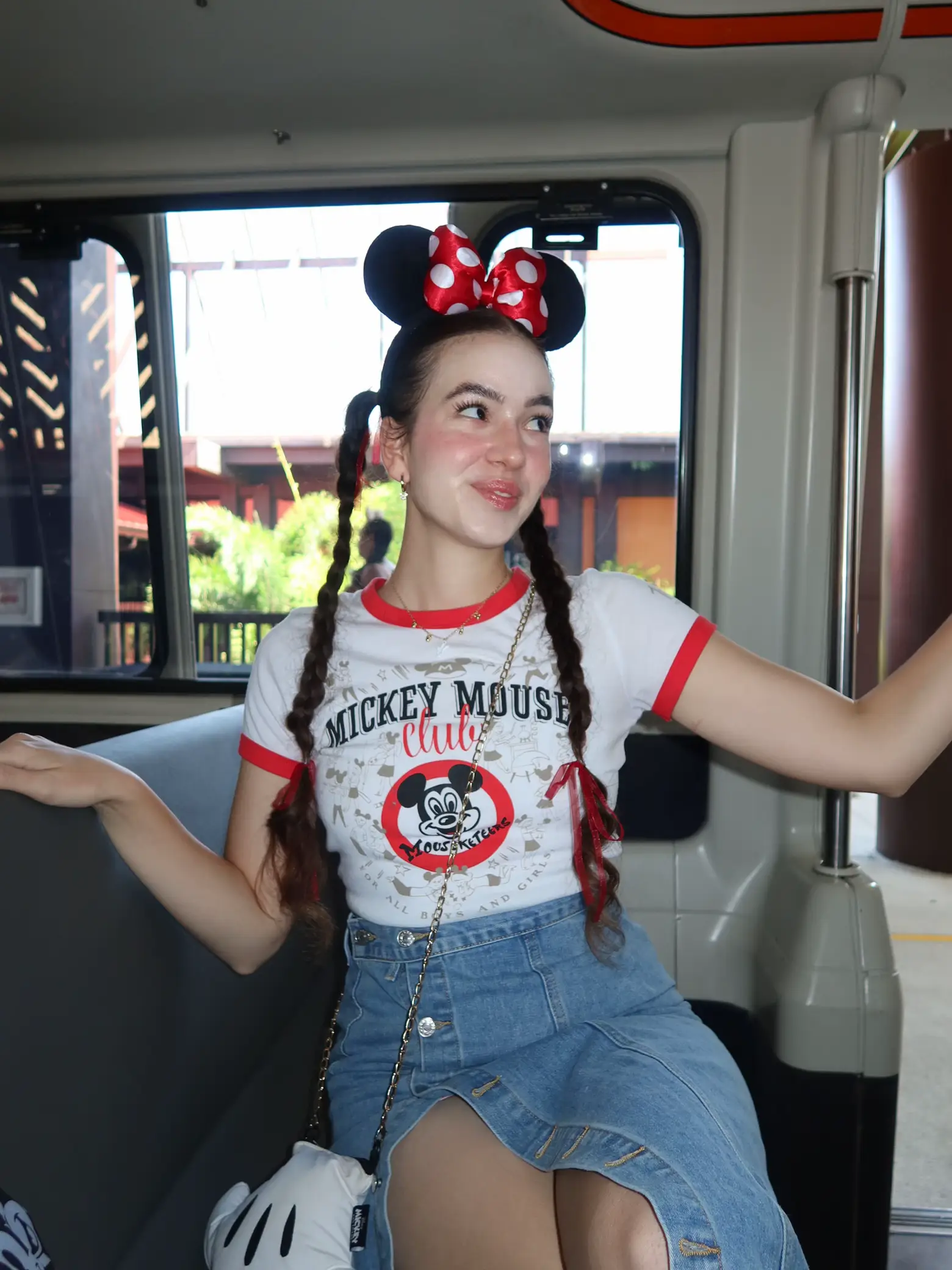  A woman wearing a Mickey Mouse shirt and jeans is sitting on a bench.