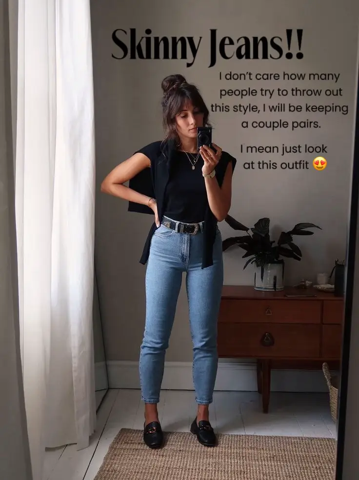  A woman in a black shirt and jeans is taking a selfie in front of a mirror.