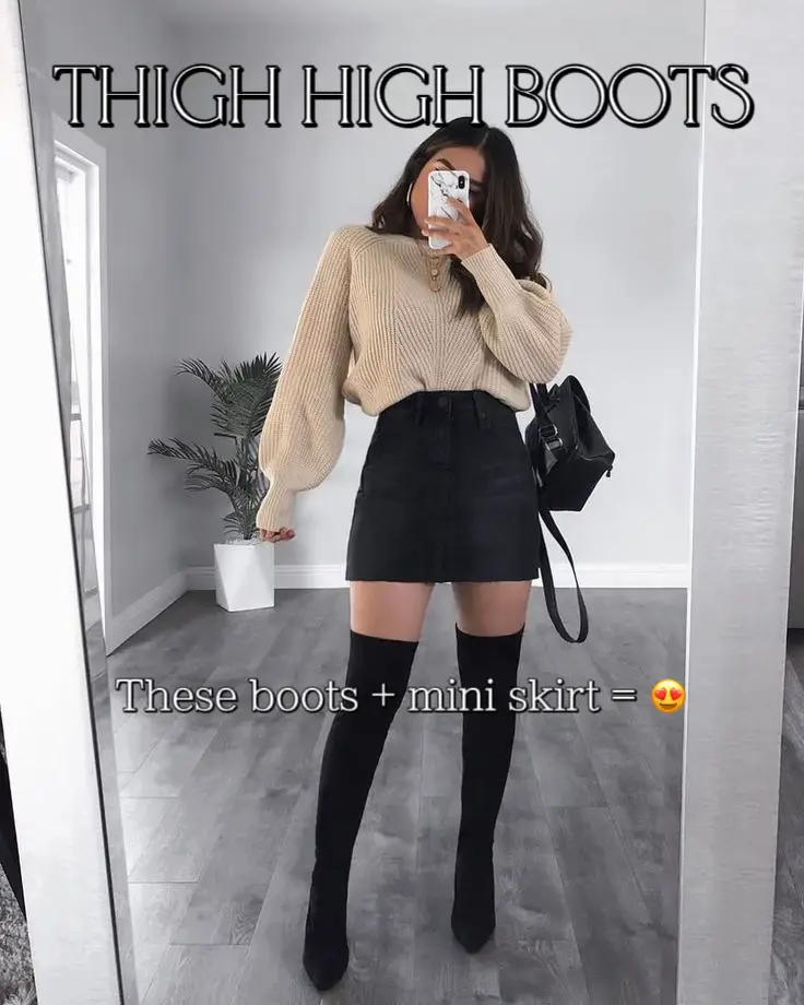  A woman wearing a white sweater and black skirt is taking a selfie in a mirror.