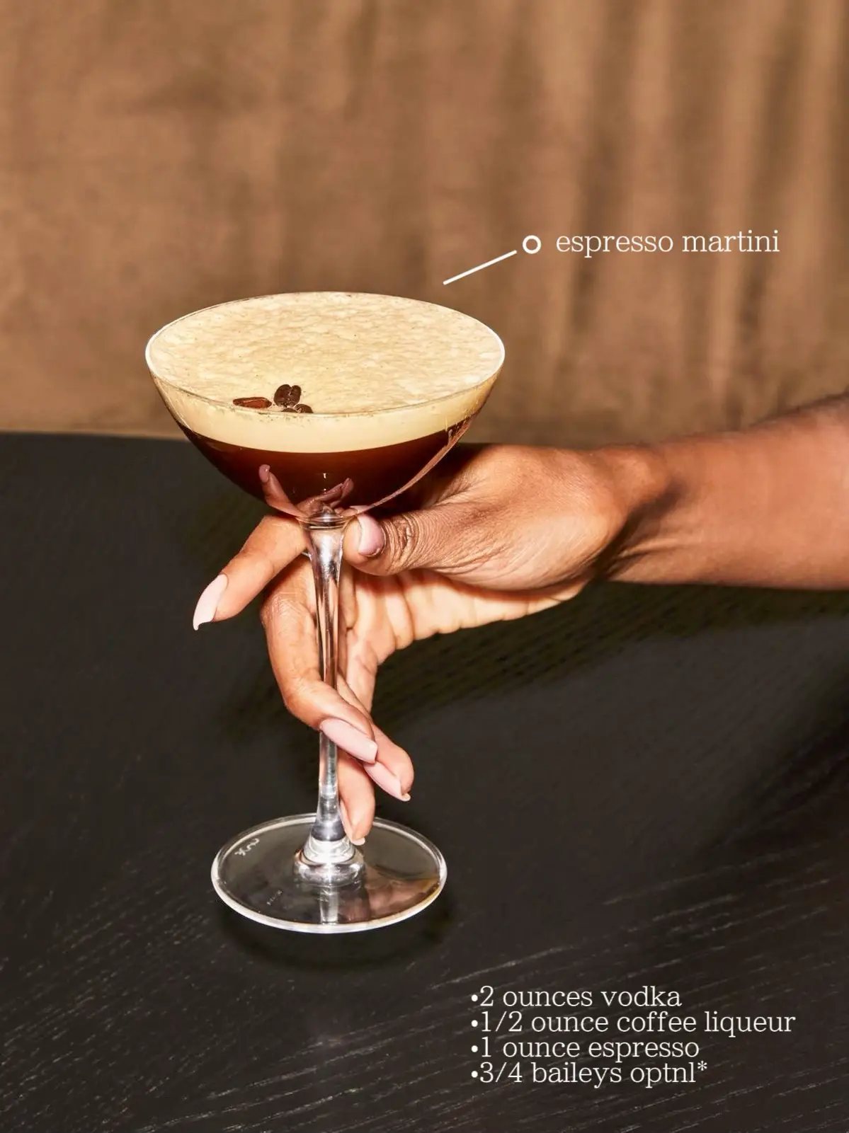  A hand holding a glass of espresso martini with a slice of lemon on top.