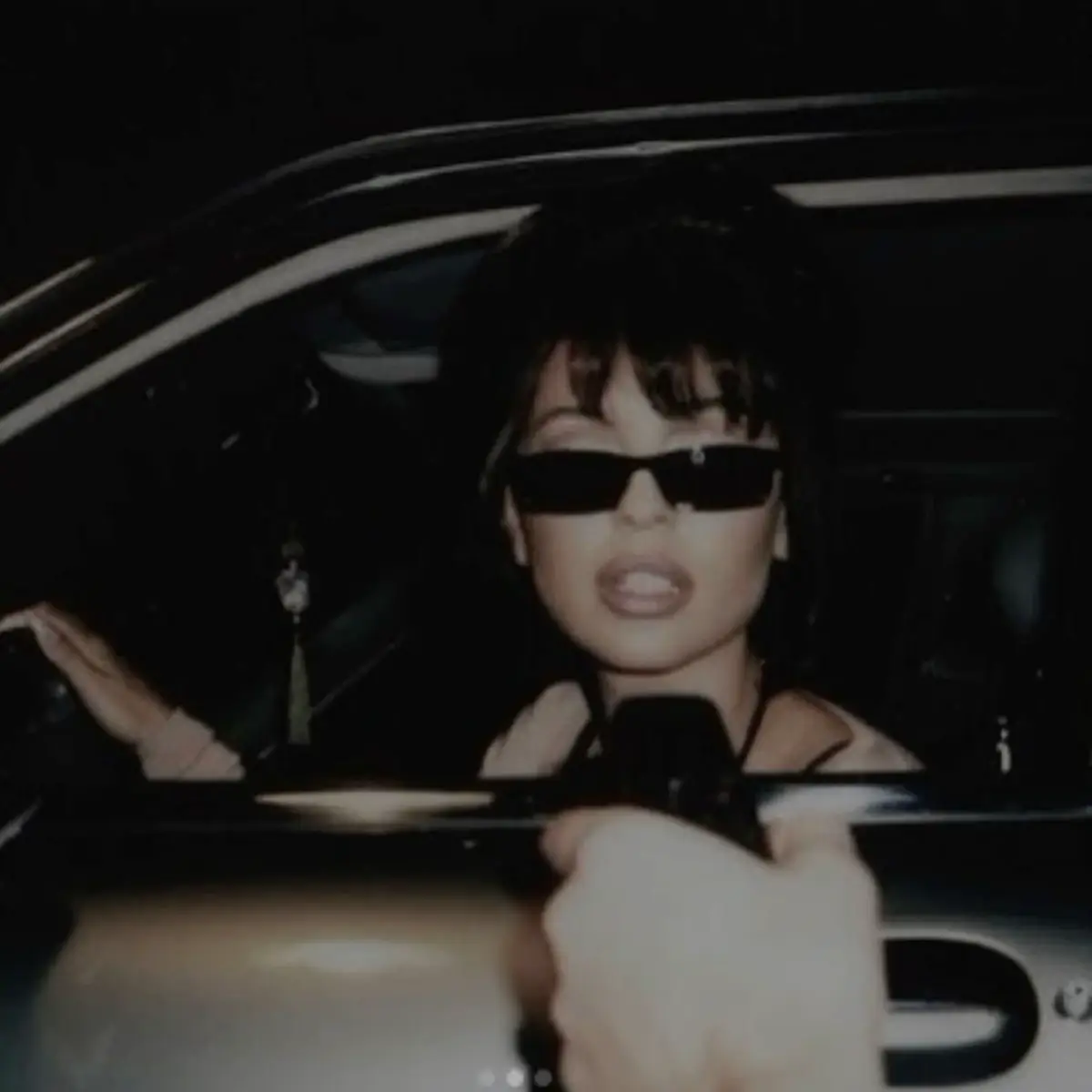  A woman wearing sunglasses and a black shirt is sitting in a car.