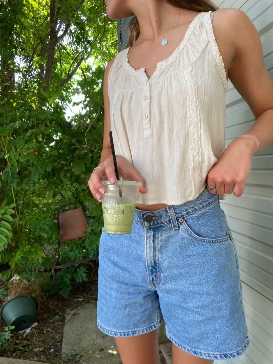  A woman wearing a brown shirt and blue shorts is holding a drink.