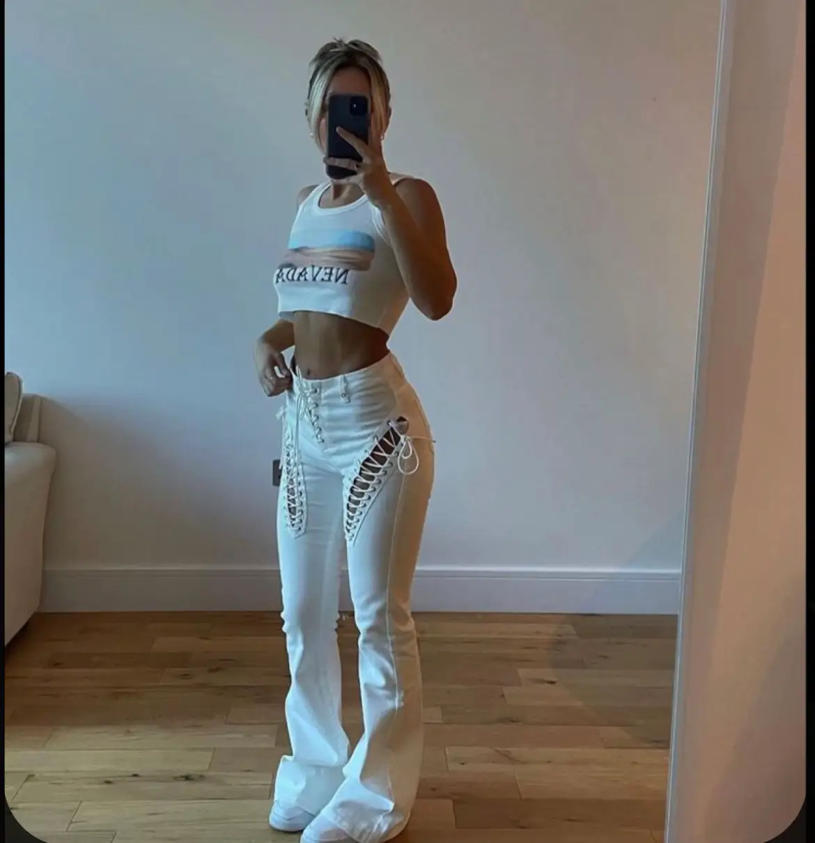  A woman in white pants and a white top is taking a selfie.