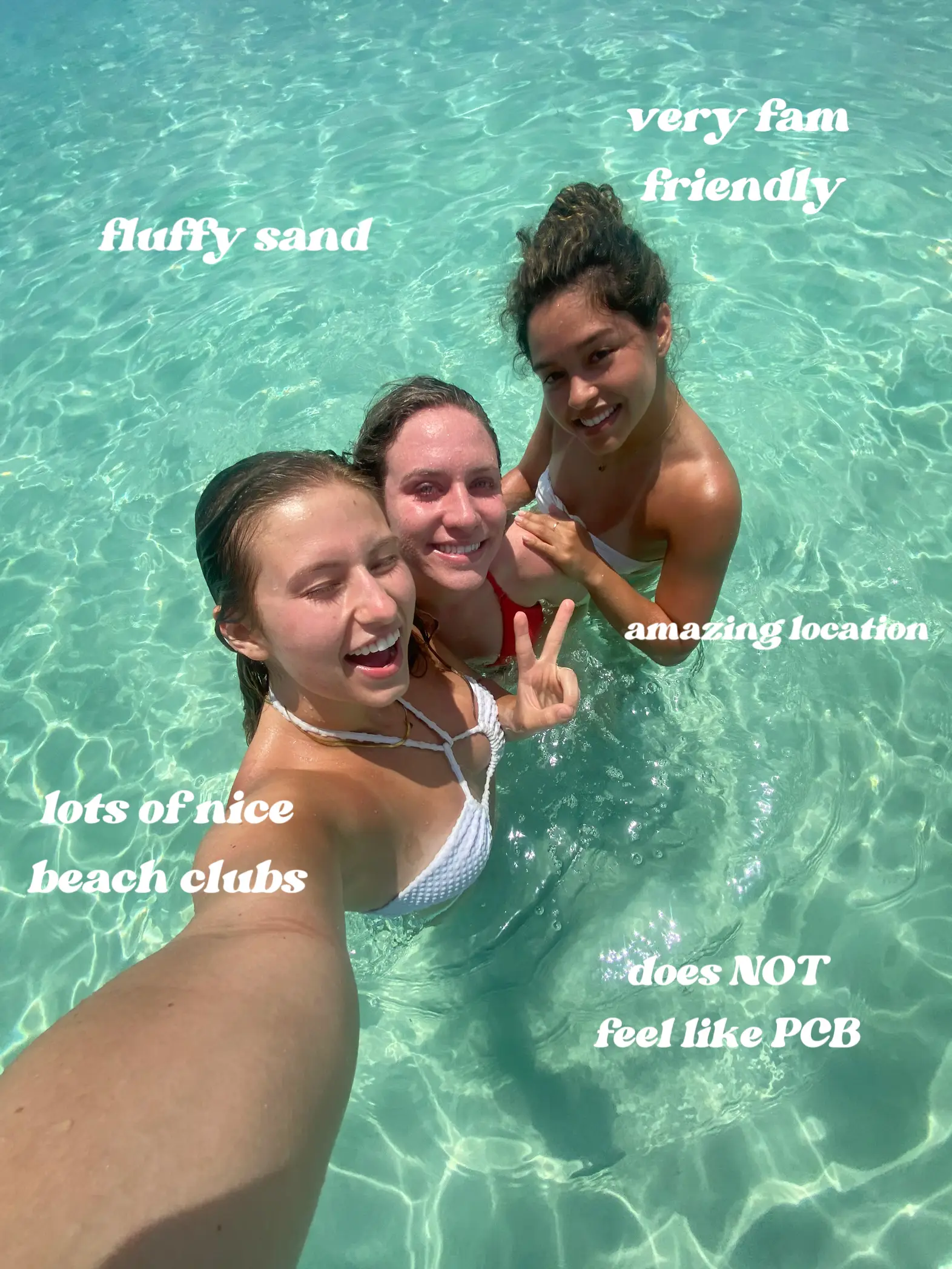  Three women are in a body of water, posing for a picture. The water is clear and blue, and they are all smiling.