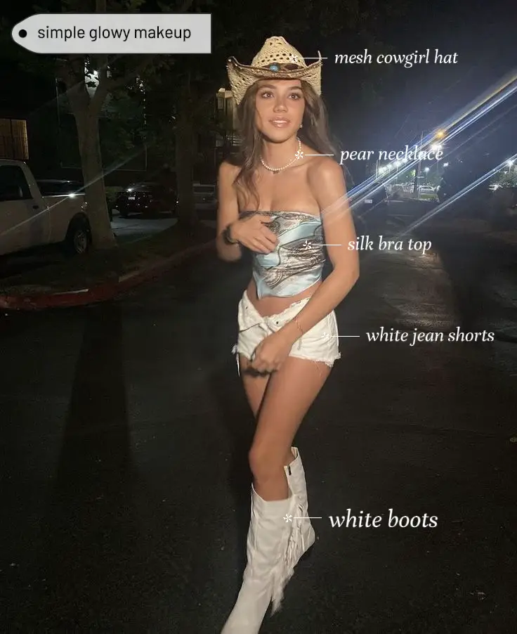  A woman wearing a cowgirl hat, silk bra top, white jean shorts, and white boots.