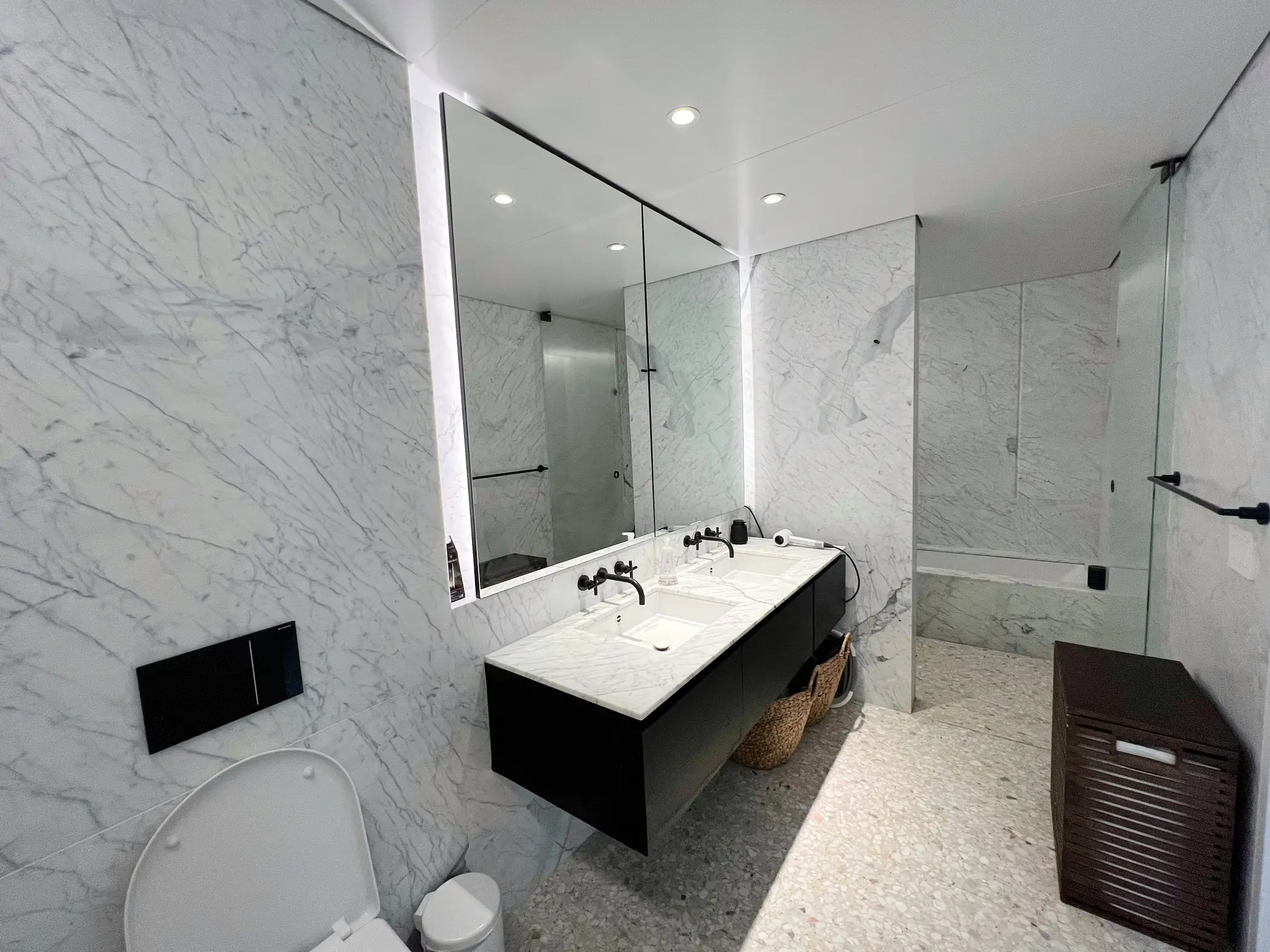  A bathroom with a sink, toilet, and mirror. The sink is white and sits under a mirror. The toilet is located to the left of the sink. The bathroom has a tile floor.