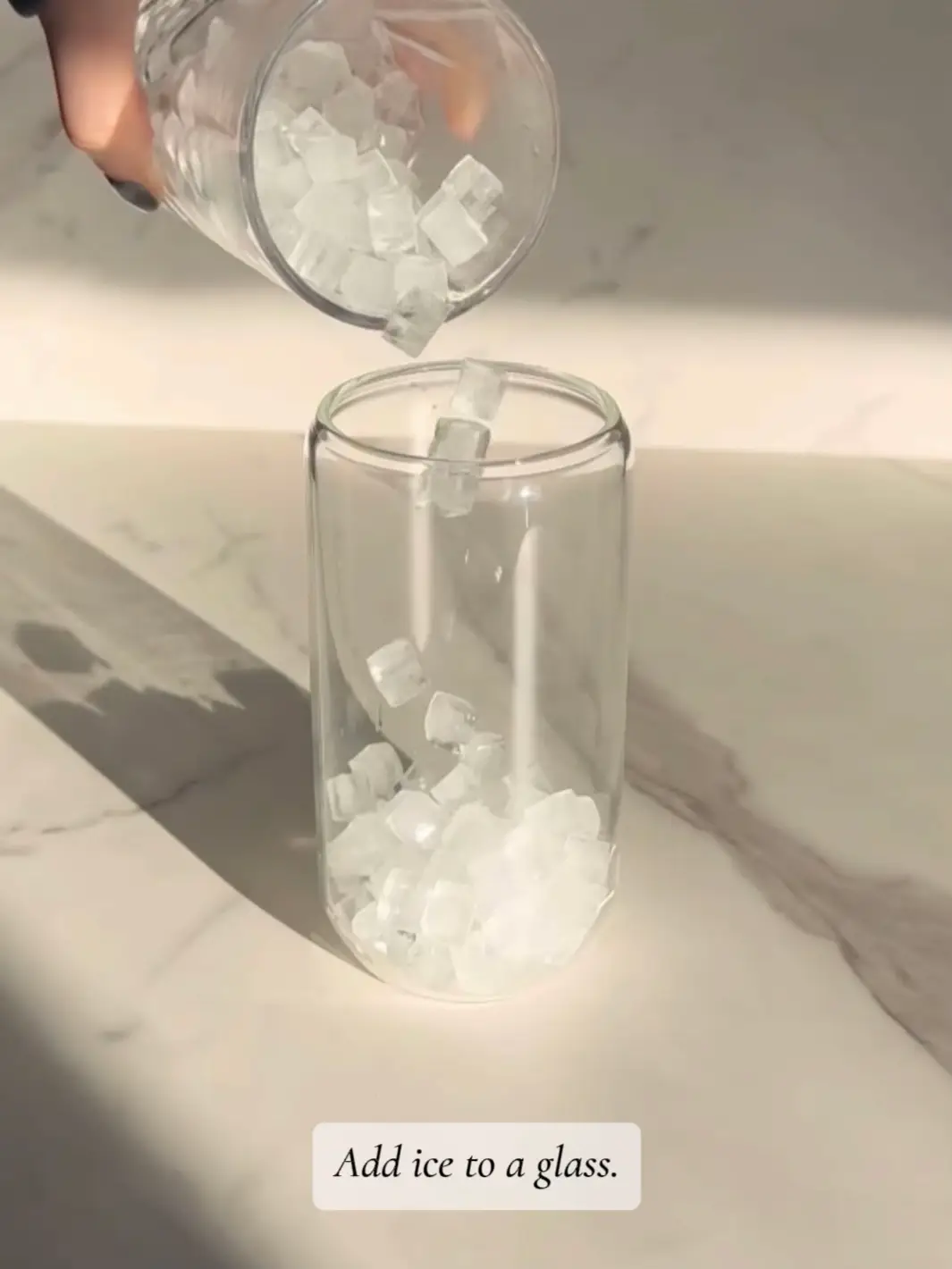  A hand holding a glass with ice and a lemon wedge.