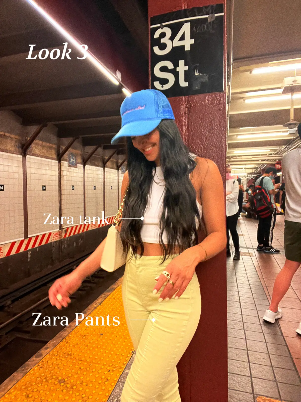  A woman wearing a blue hat and a grey shirt is standing next to a subway train. She is wearing a blue hat and jeans.