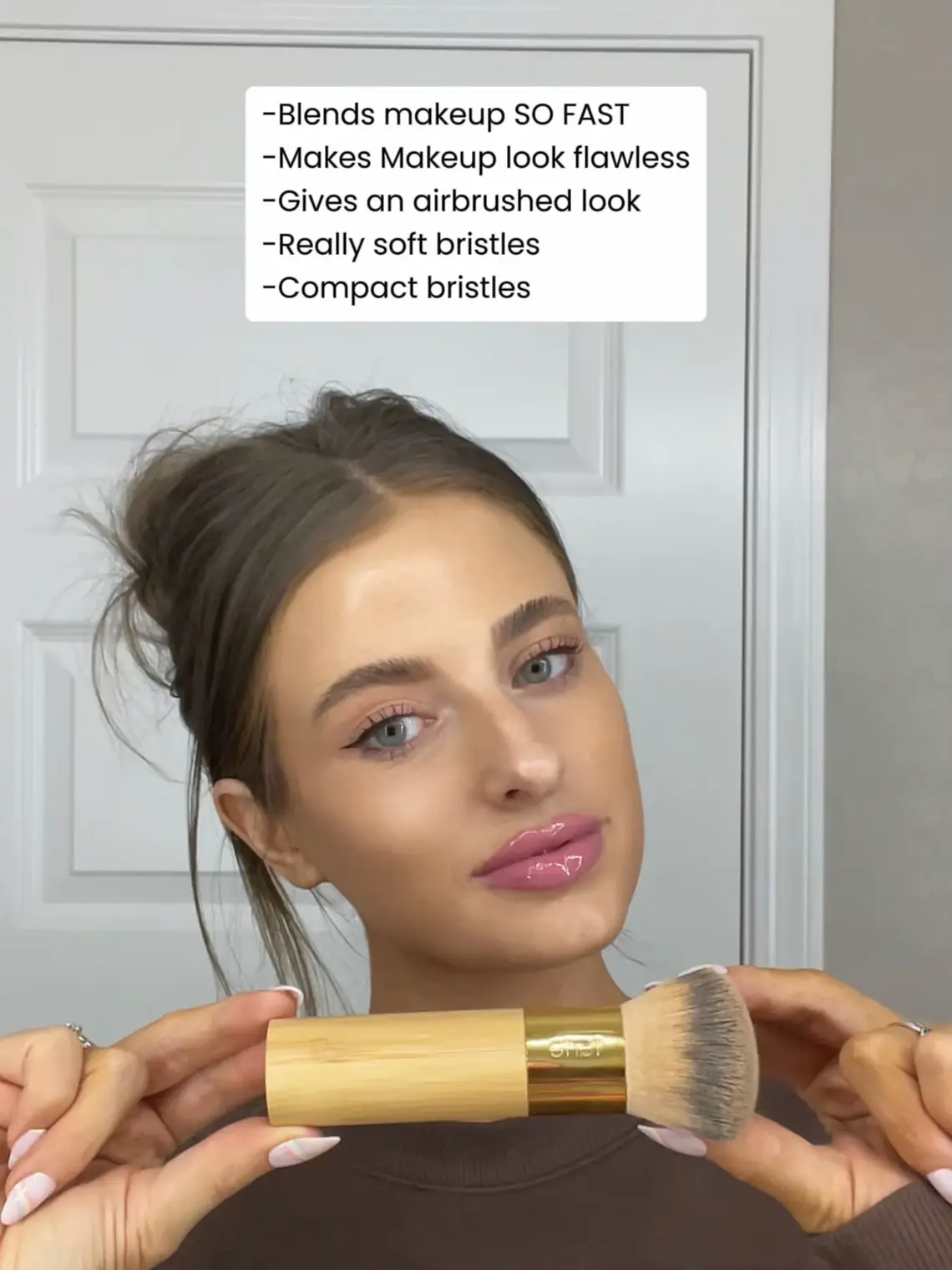  A woman is holding a makeup brush in front of her face.