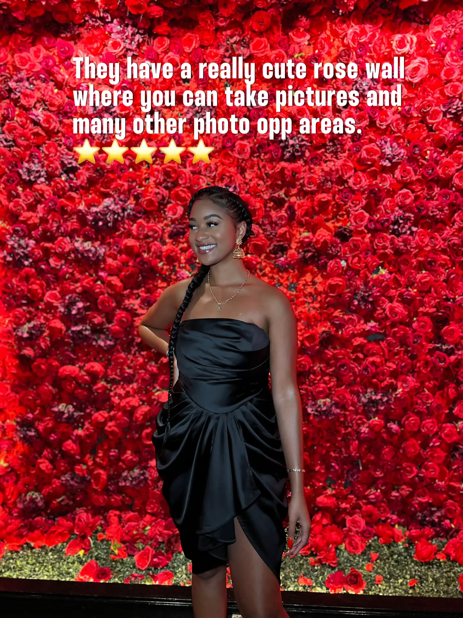  A woman wearing a black dress is standing in front of a rose wall.